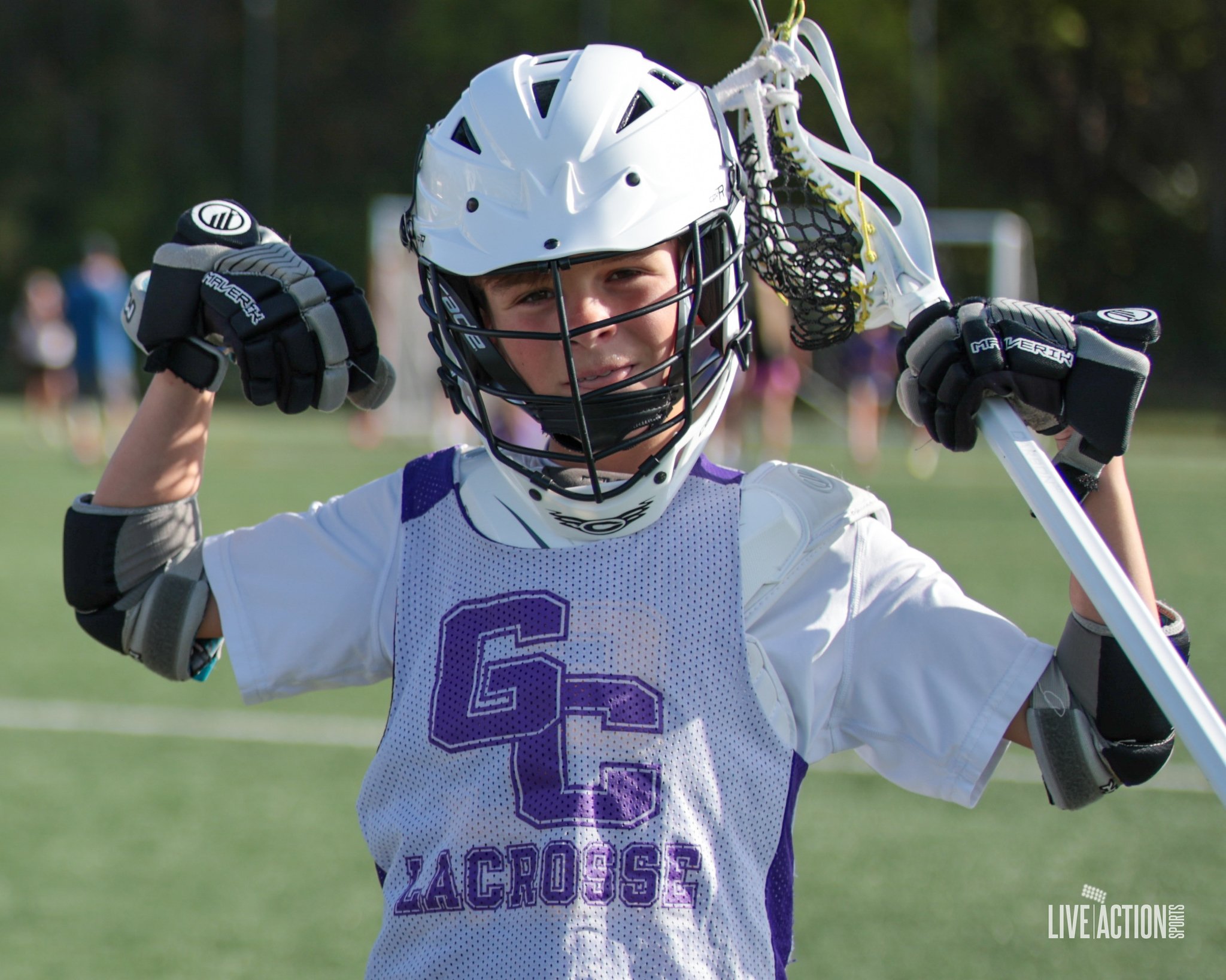 Junior Golden Eagles boy in lacrosse gear holding lacrosse stick and smiling on the field
