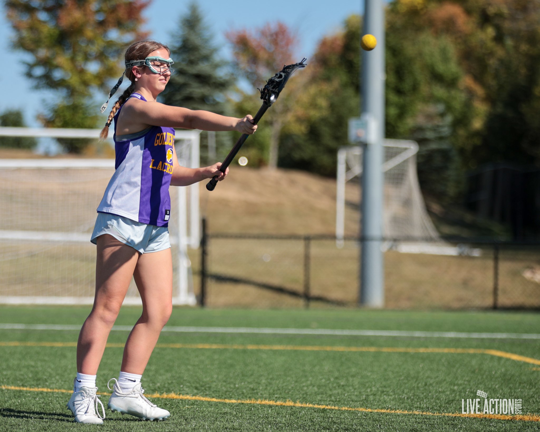 A female lacrosse player preparing to catch the ball on a grassy field